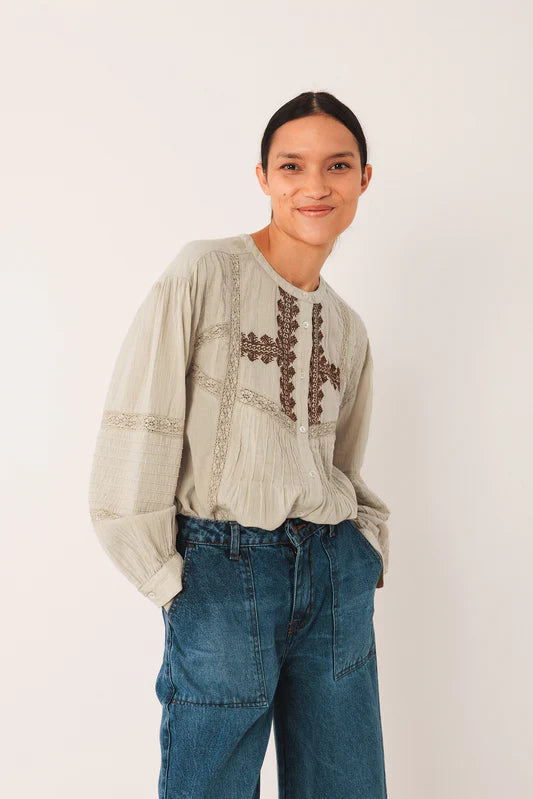 Woman wearing a beige blouse with embroidery and blue jeans on a white background