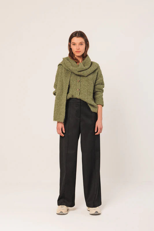 Woman wearing a green sweater and black pants on a white background