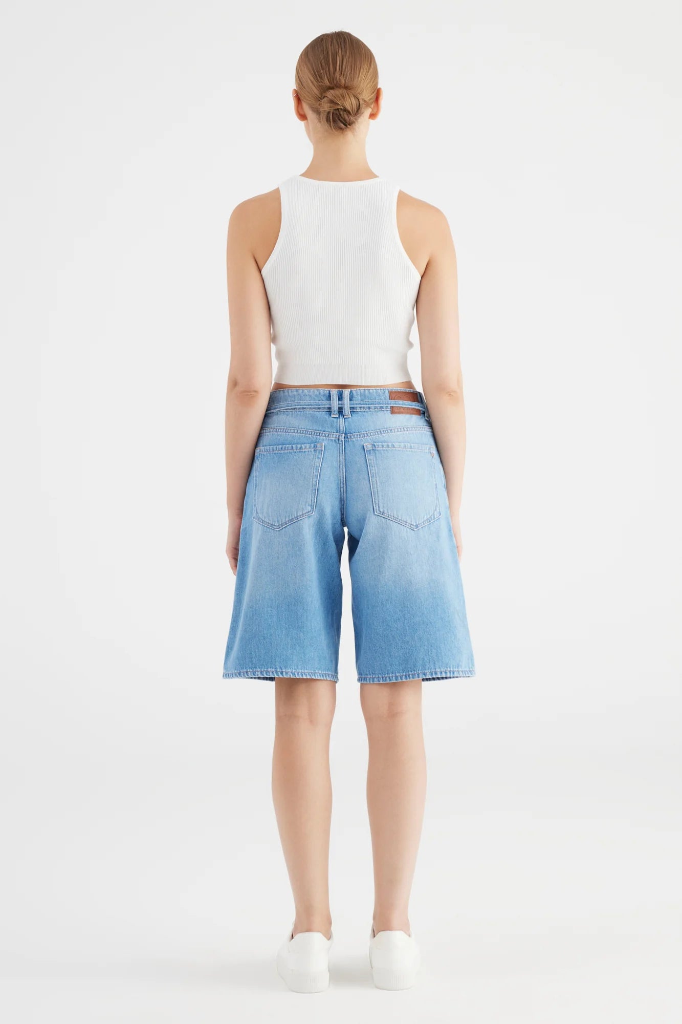 Person wearing a white sleeveless top and light blue denim shorts on a white background
