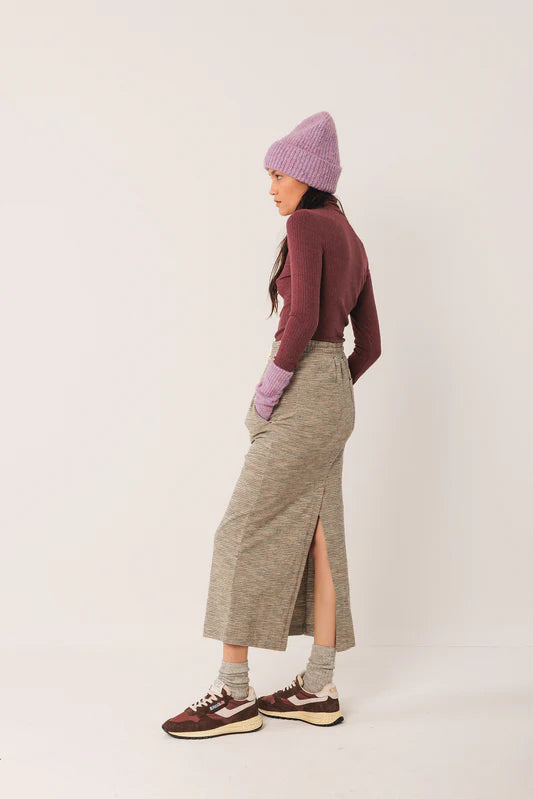 Person wearing a maroon sweater, gray skirt, and purple beanie on a white background