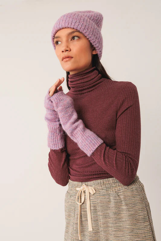 Person wearing a maroon turtleneck sweater, lavender beanie, gloves, and plaid pants against a white background