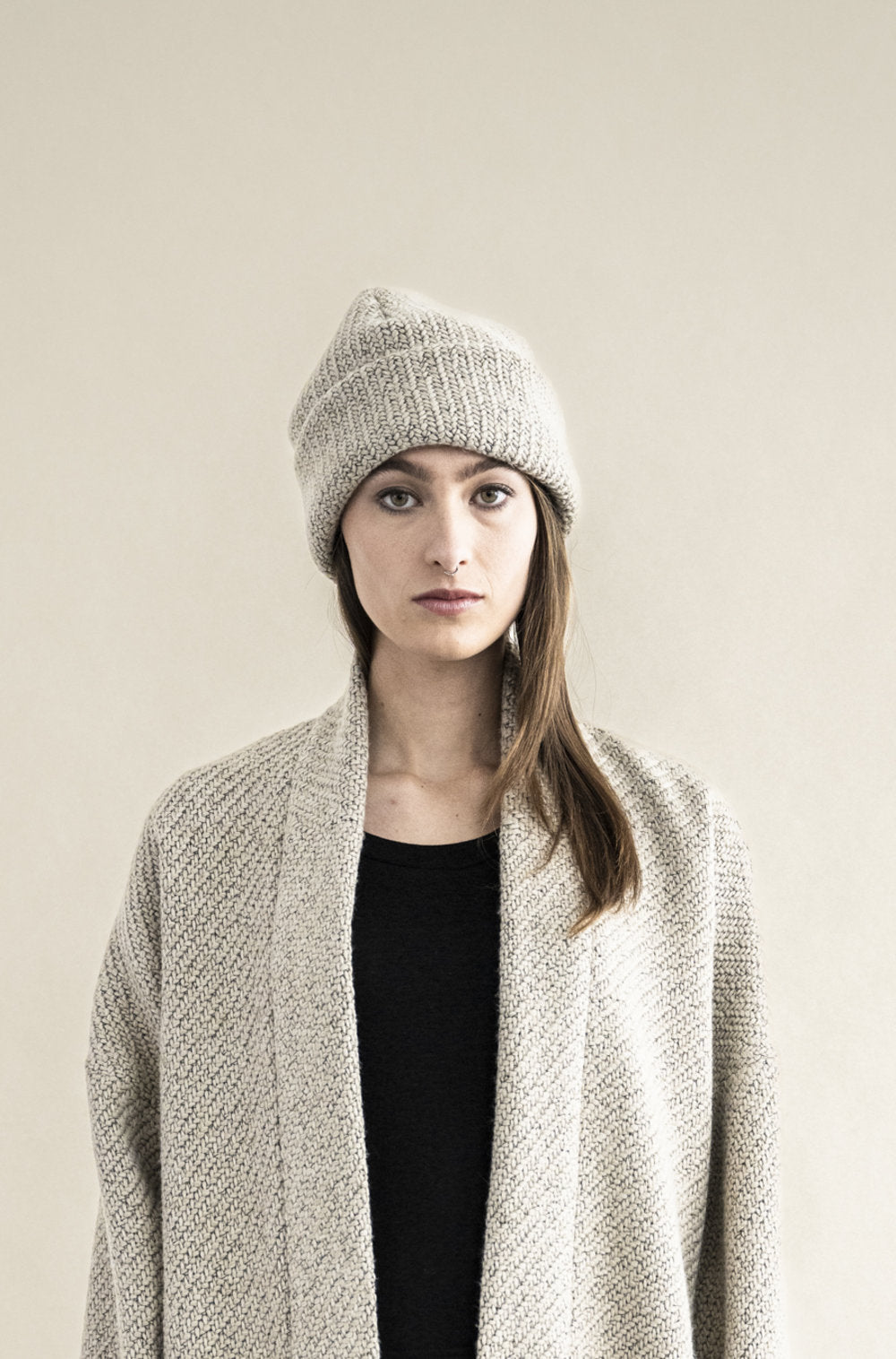 Woman wearing a gray knit beanie and light gray cardigan against a beige background