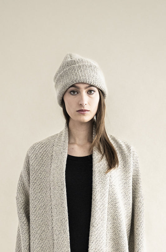 Woman wearing a gray knit beanie and light gray cardigan against a beige background