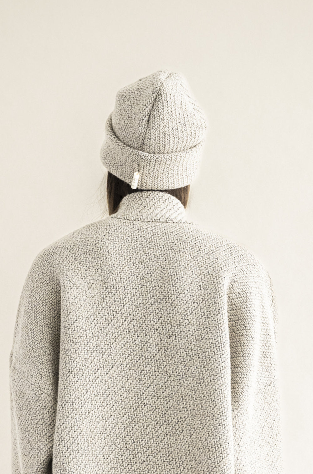 Person wearing a textured gray sweater and knit beanie against a plain background