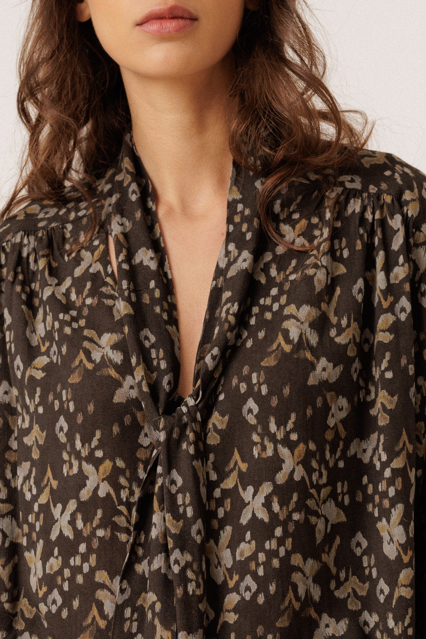 Close-up of a woman wearing a dark gray blouse with a beige and gray blue abstract floral pattern and a tie-neck detail.