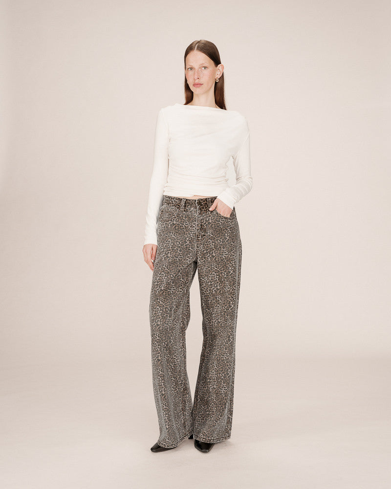 Woman wearing a white sweater and patterned pants on a plain background