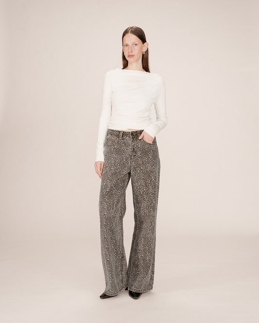 Woman wearing a white sweater and patterned pants on a plain background