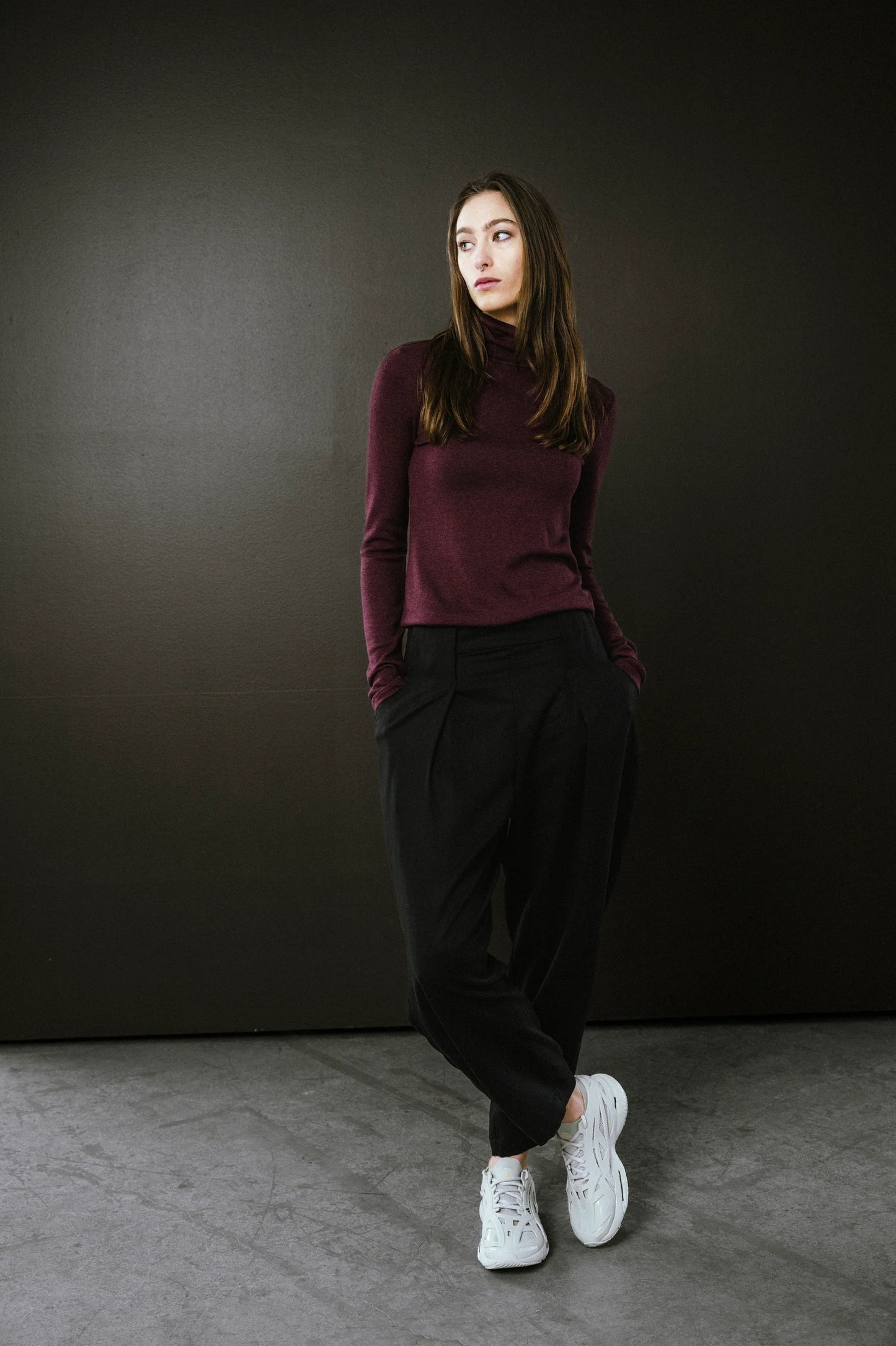 Person wearing a burgundy turtleneck and black pants against a dark background