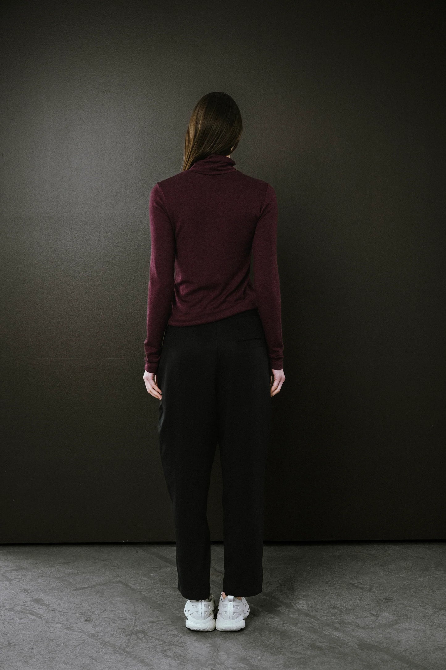 Person wearing a burgundy long-sleeve top and black pants against a dark background