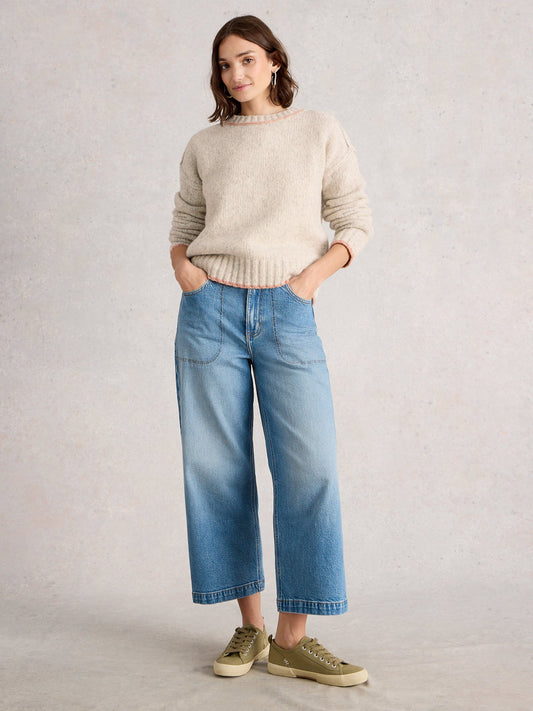 Woman wearing a beige sweater and blue jeans against a plain background