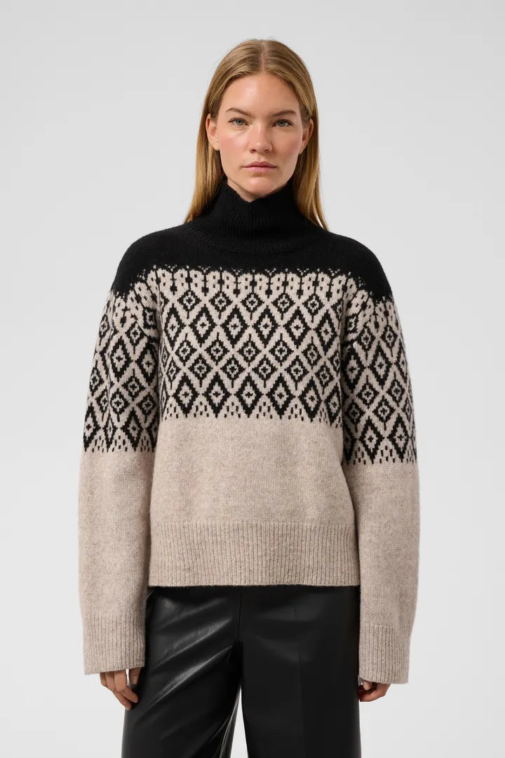 Woman wearing black and oatmeal Fair Isle turtleneck sweater by Soaked in Luxury, paired with black leather pants