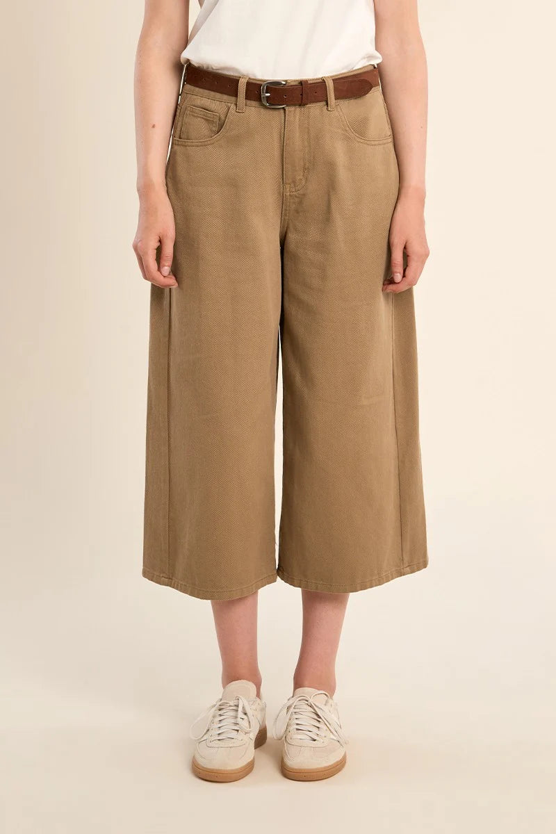 Person wearing beige wide-leg pants with a brown belt on a beige background