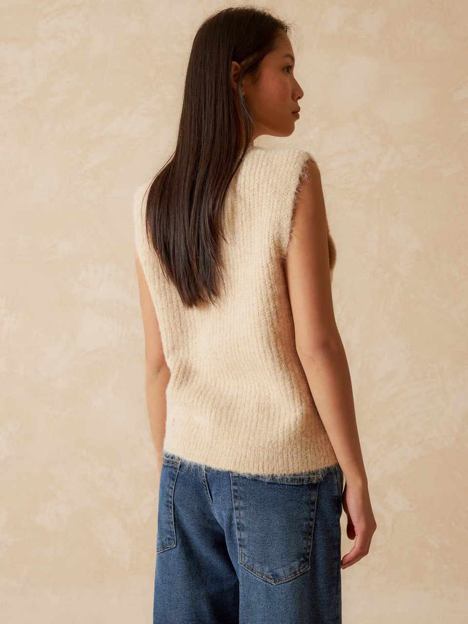 Elevate your style with this knitted vest cardigan by Indi &amp; Cold. Its sleek design and beutiful cream colour allows for easy layering over a tee or lightweight sweater. The shoulder placement and wide armholes provide flexibility. Fasten it with the charming button closure in the front. The playful ribbed fabric adds a unique touch.