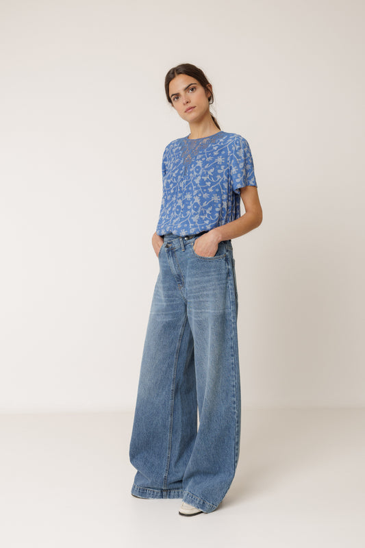 Woman wearing a blue patterned top and wide-leg jeans on a white background
