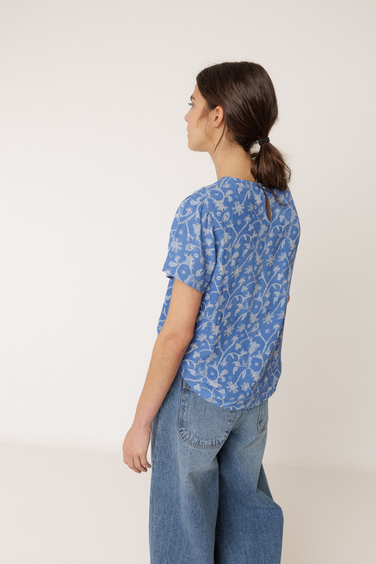 Person wearing a blue patterned shirt and jeans against a white background