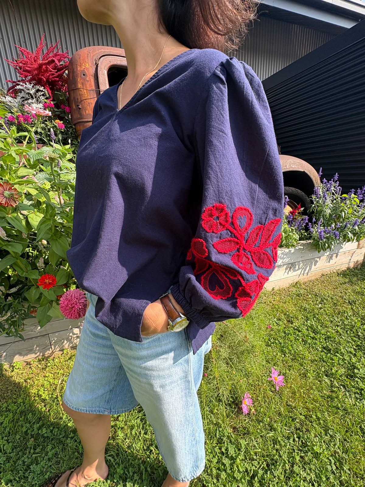 Woman wearing navy blouse with red floral embroidered sleeve by ICHI, paired with denim shorts