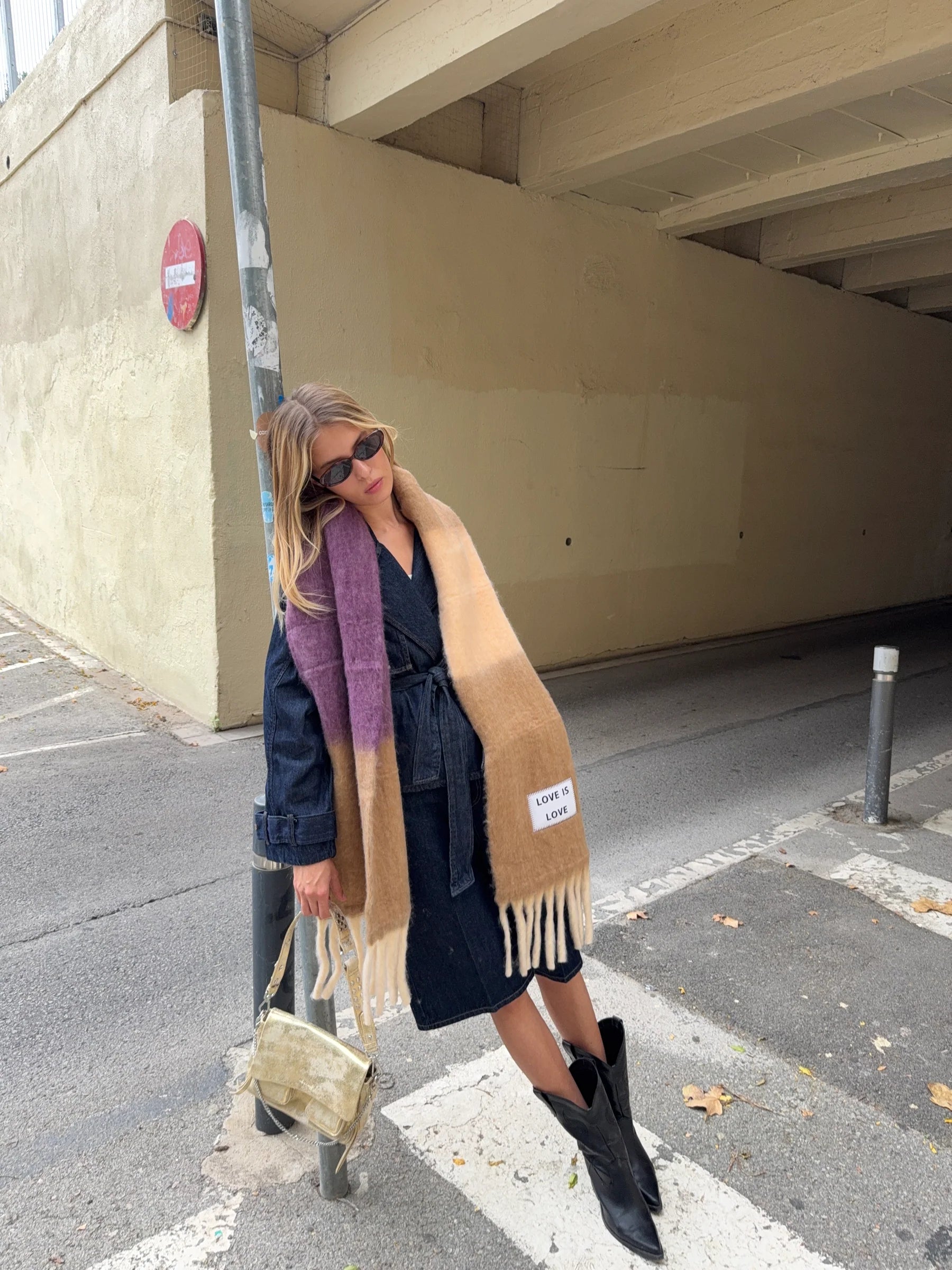 Woman standing on a street corner wearing a long scarf and dark coat.