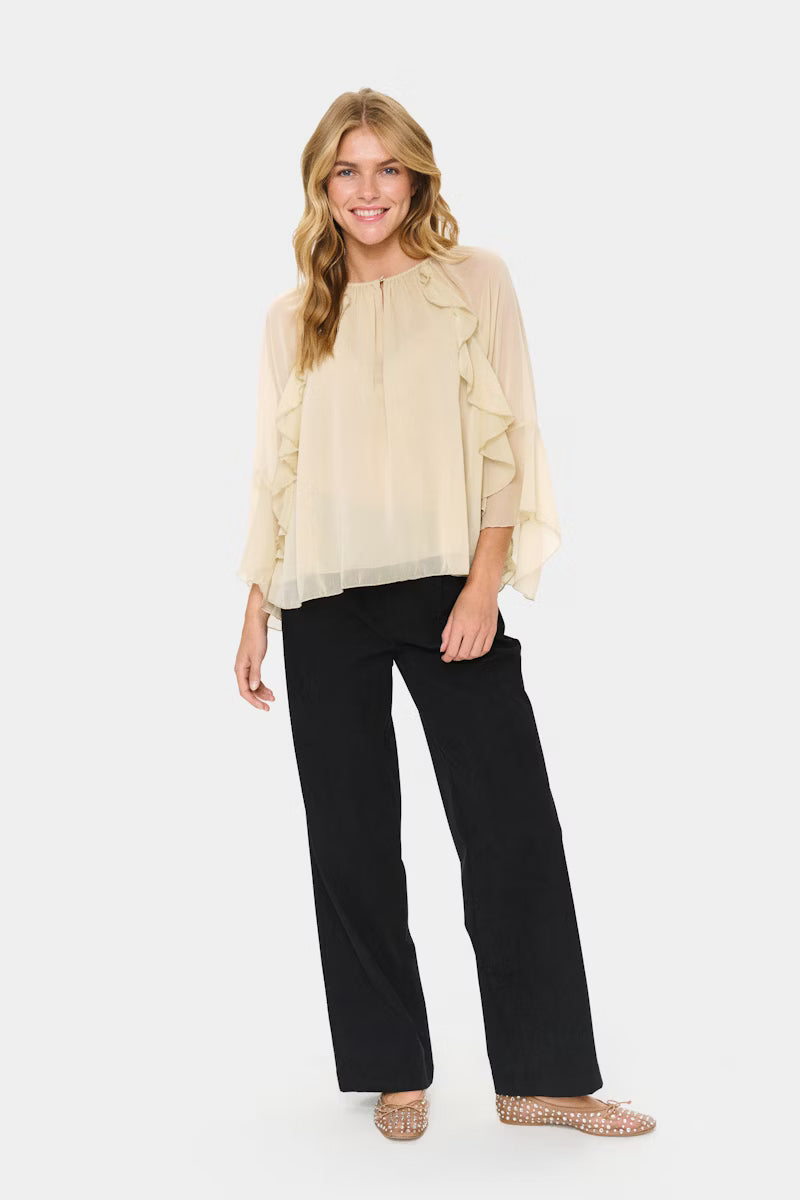 Woman wearing a light beige blouse and black pants on a white background