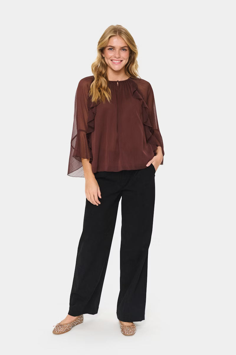 Woman wearing a brown blouse and black pants on a white background