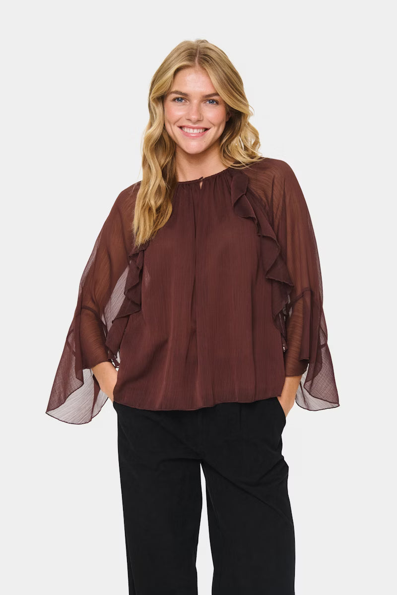 Woman wearing a brown blouse with sheer sleeves on a white background