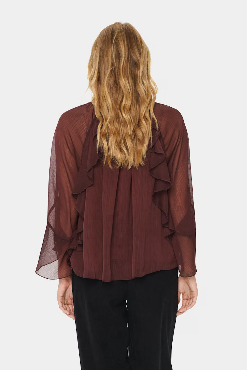 Woman wearing a burgundy blouse with ruffled sleeves on a white background