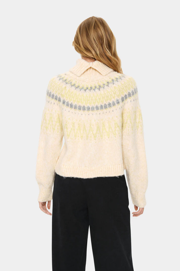 Woman wearing a cream-colored sweater with patterned shoulders on a white background