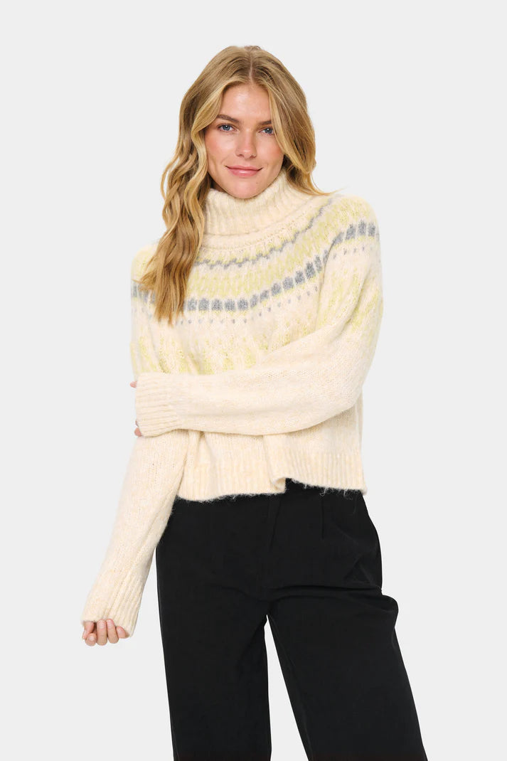 Woman wearing a cream-colored sweater with a patterned design on a white background
