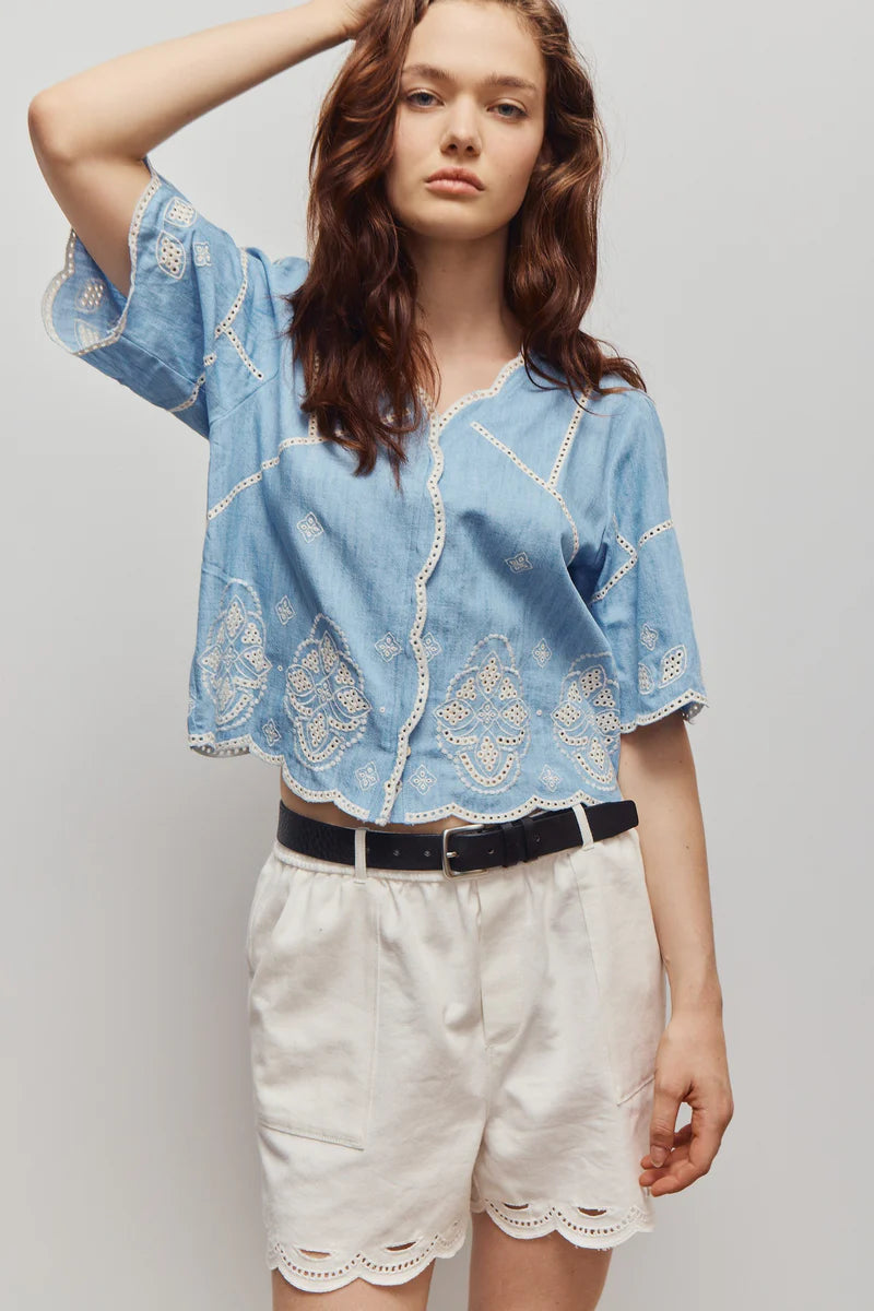 Woman wearing a blue embroidered blouse and white shorts on a plain background