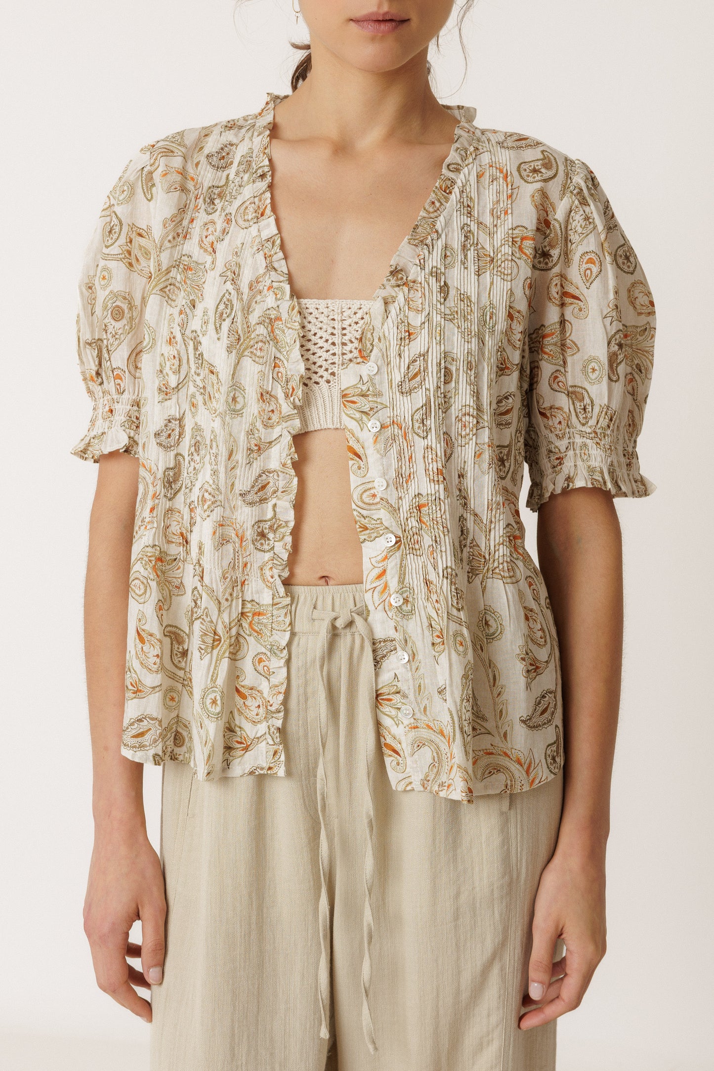 Woman wearing a patterned top and light pants on a white background