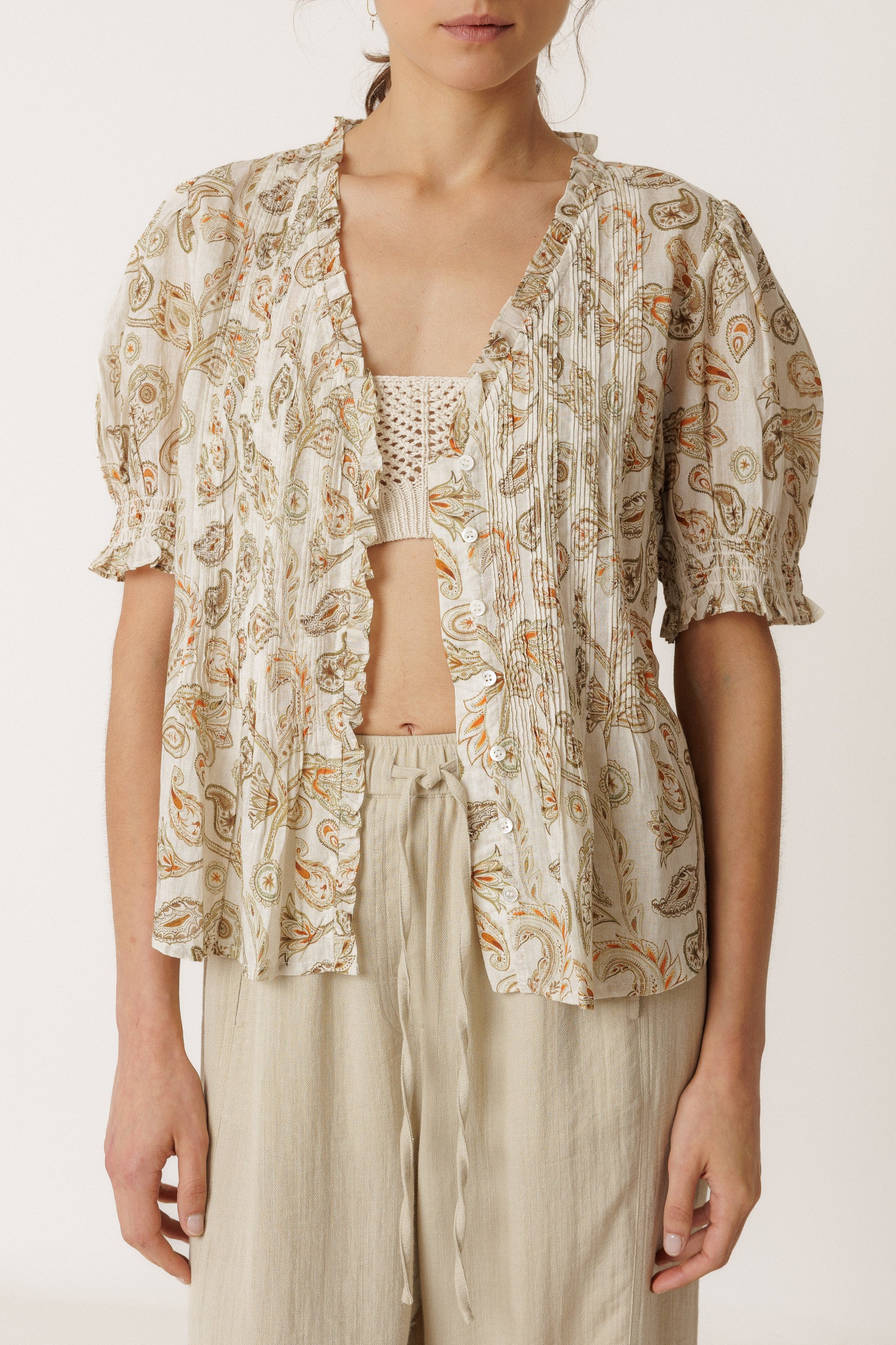 Woman wearing a patterned top and light pants on a white background