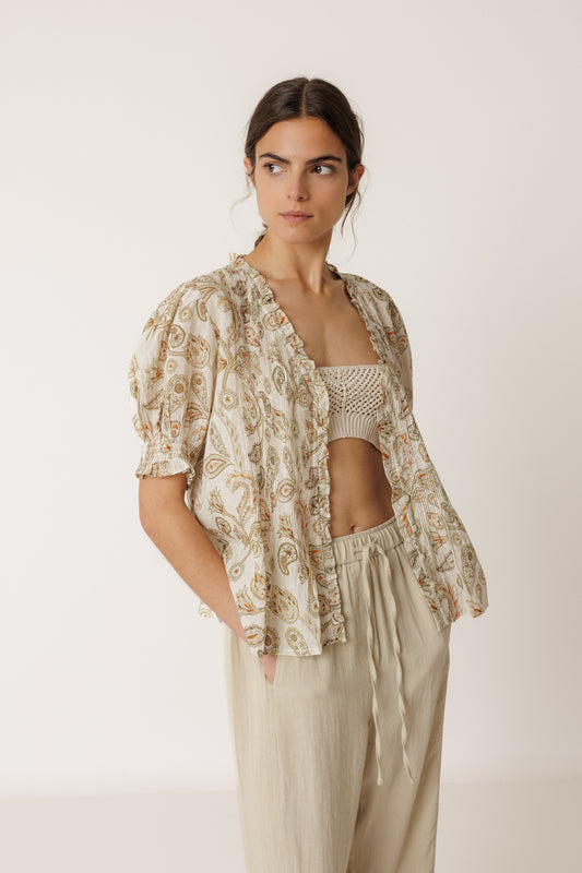 Woman wearing a patterned top and beige pants against a white background