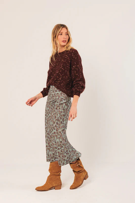 Woman wearing a patterned sweater and skirt with brown boots on a white background