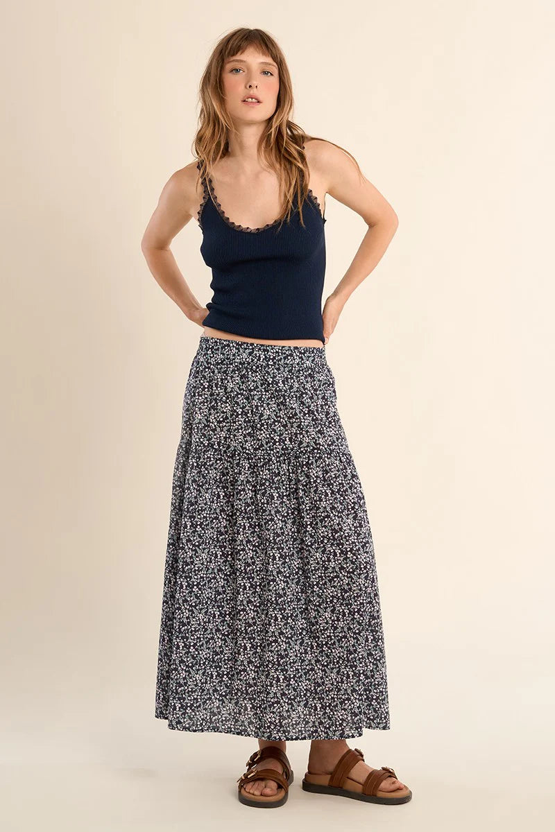 Woman wearing a navy tank top and patterned skirt on a beige background