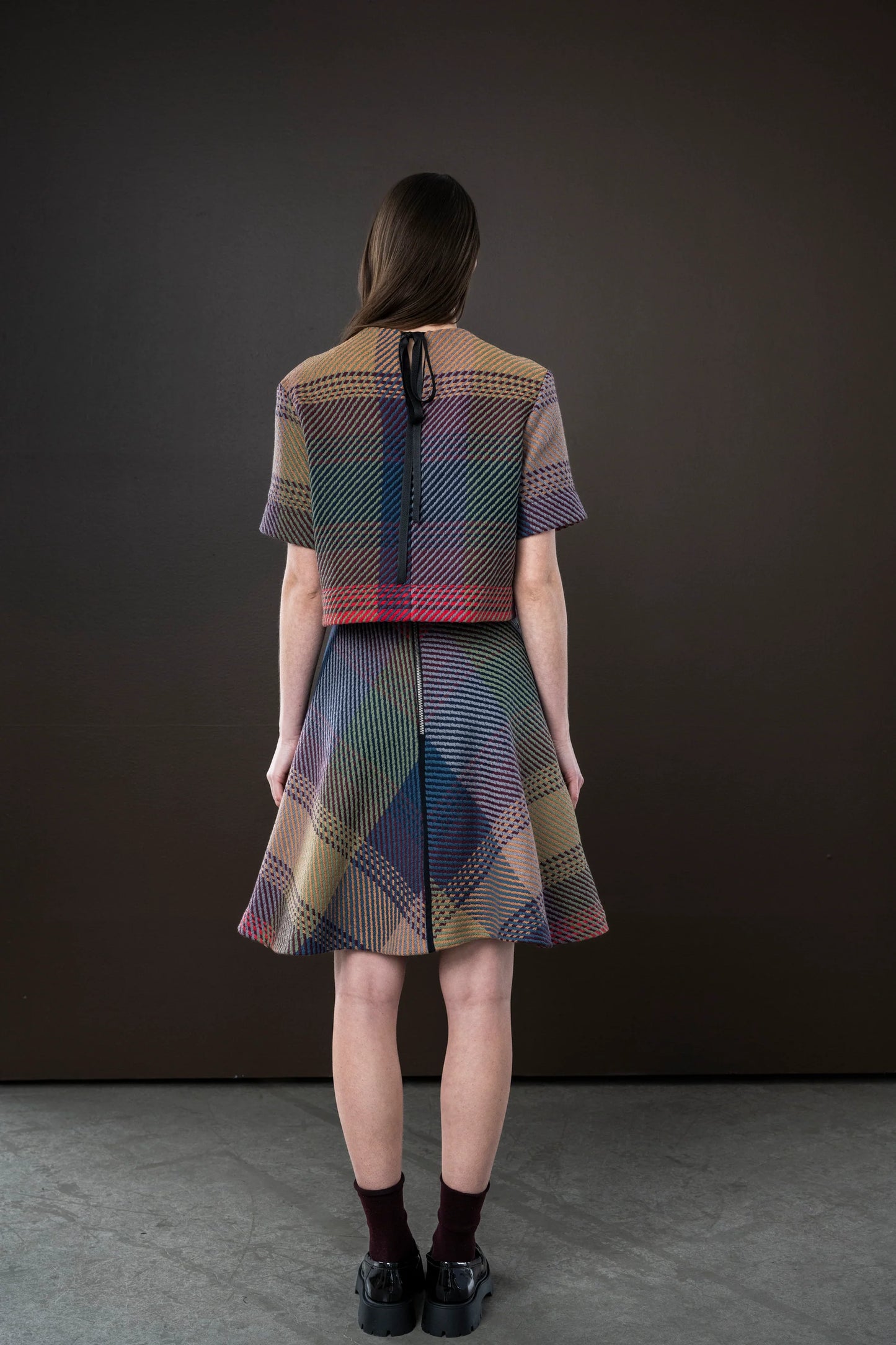 Woman wearing a colorful checkered dress and top against a dark background