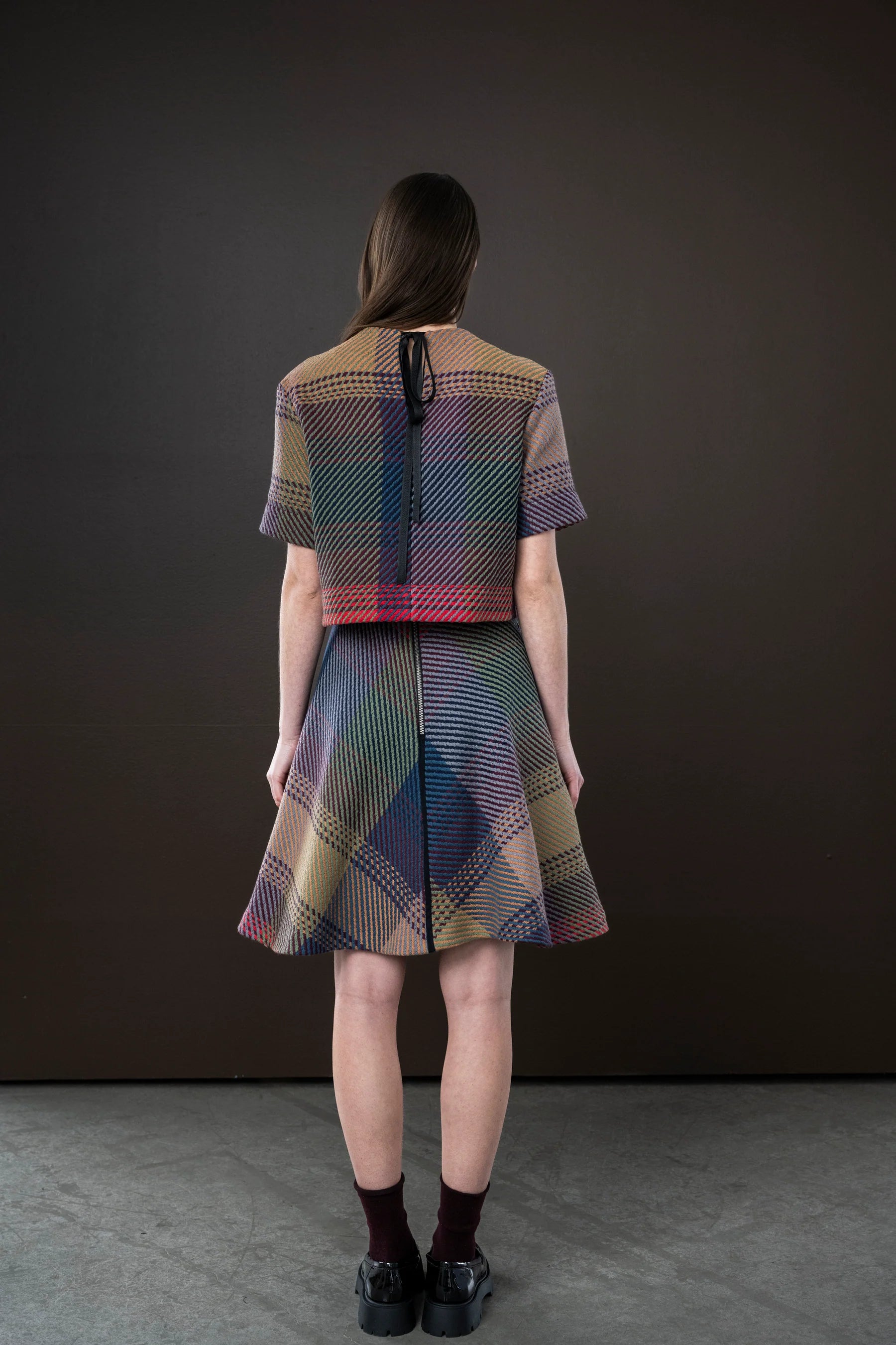 Woman wearing a colorful checkered dress and top against a dark background