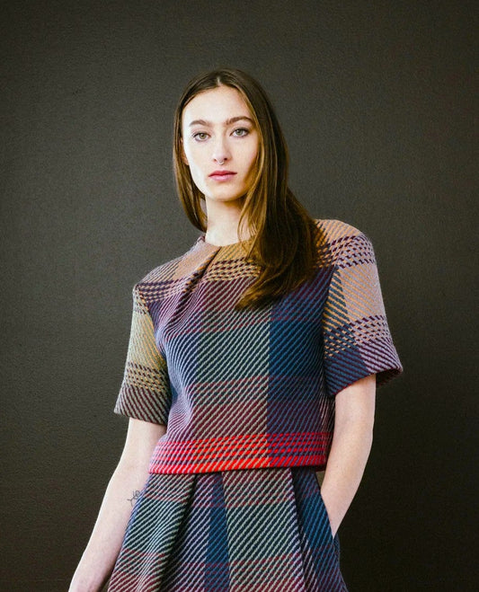Woman wearing a plaid dress standing against a dark wall.