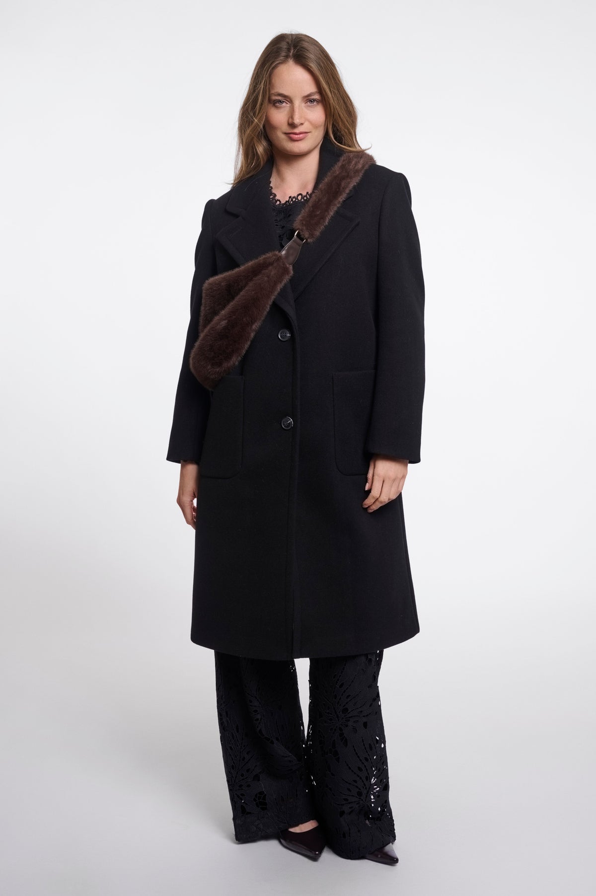 Rino & Pelle Nayla chocolate brown faux fur crescent crossbody bag worn across the body over a black wool coat