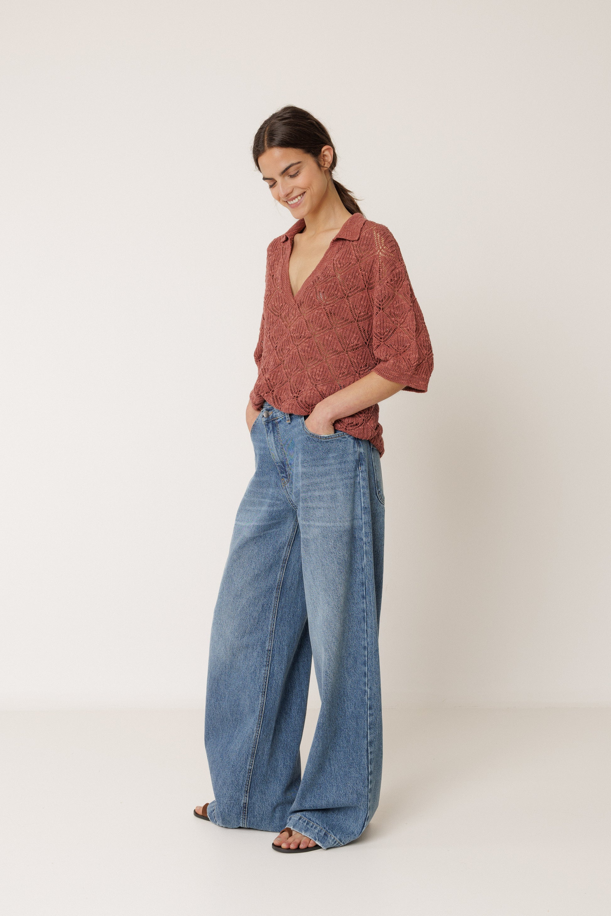 Woman wearing a rust-colored open knit polo and blue jeans on a white background