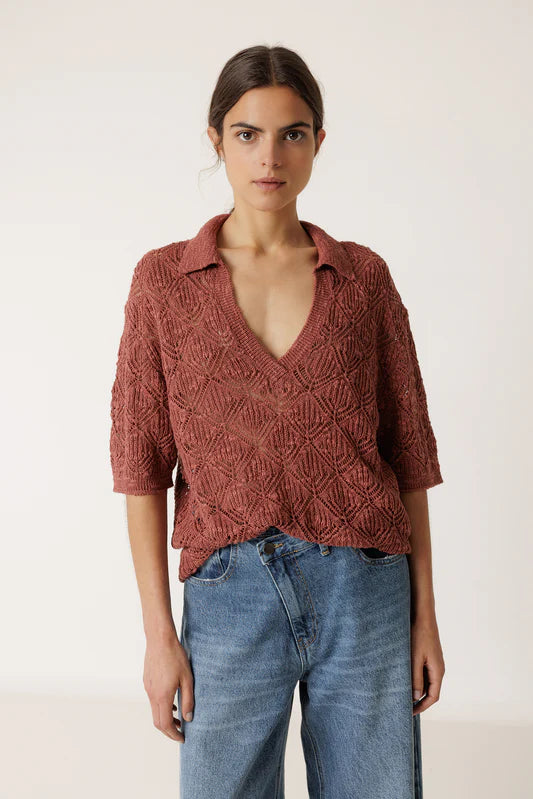 Woman wearing a rust-colored knitted shirt and blue jeans on a white background