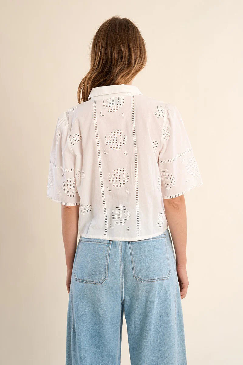 Person wearing a white lace top and blue jeans on a beige background
