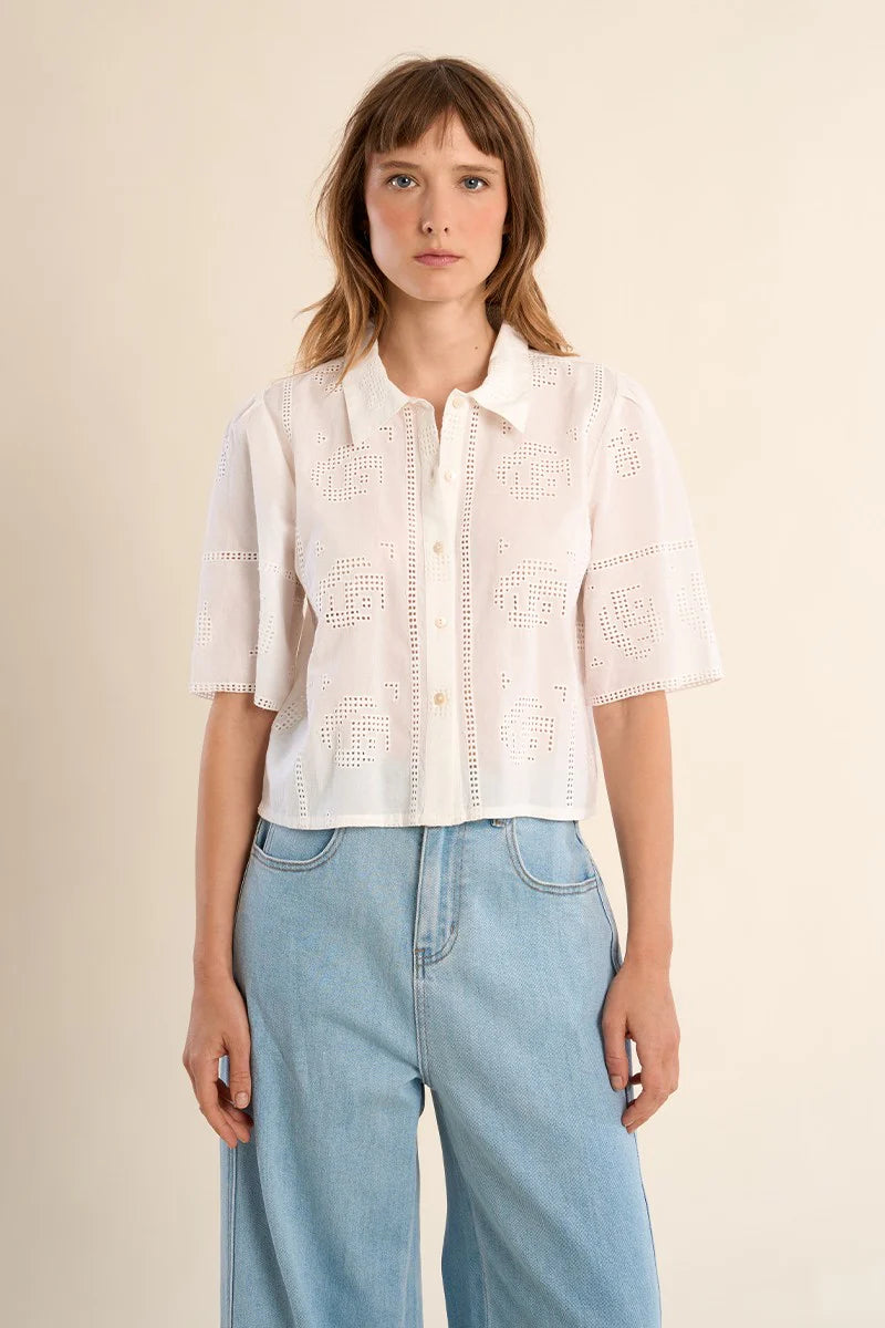 Woman wearing a white blouse and blue jeans against a beige background