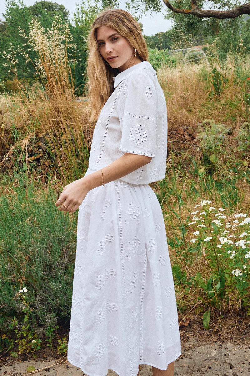 Woman in a white dress standing in a natural setting with plants and flowers.