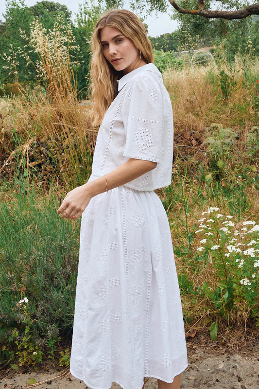 Woman in a white dress standing in a natural setting with plants and flowers.