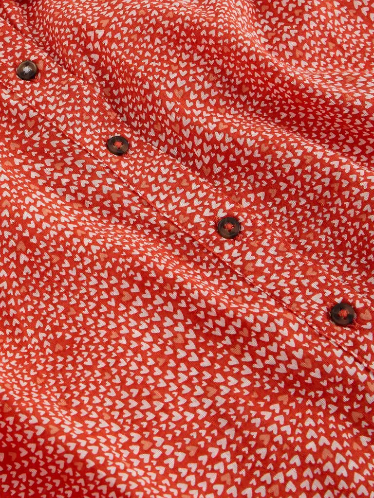 Close-up of a red fabric with white pattern and metal buttons.
