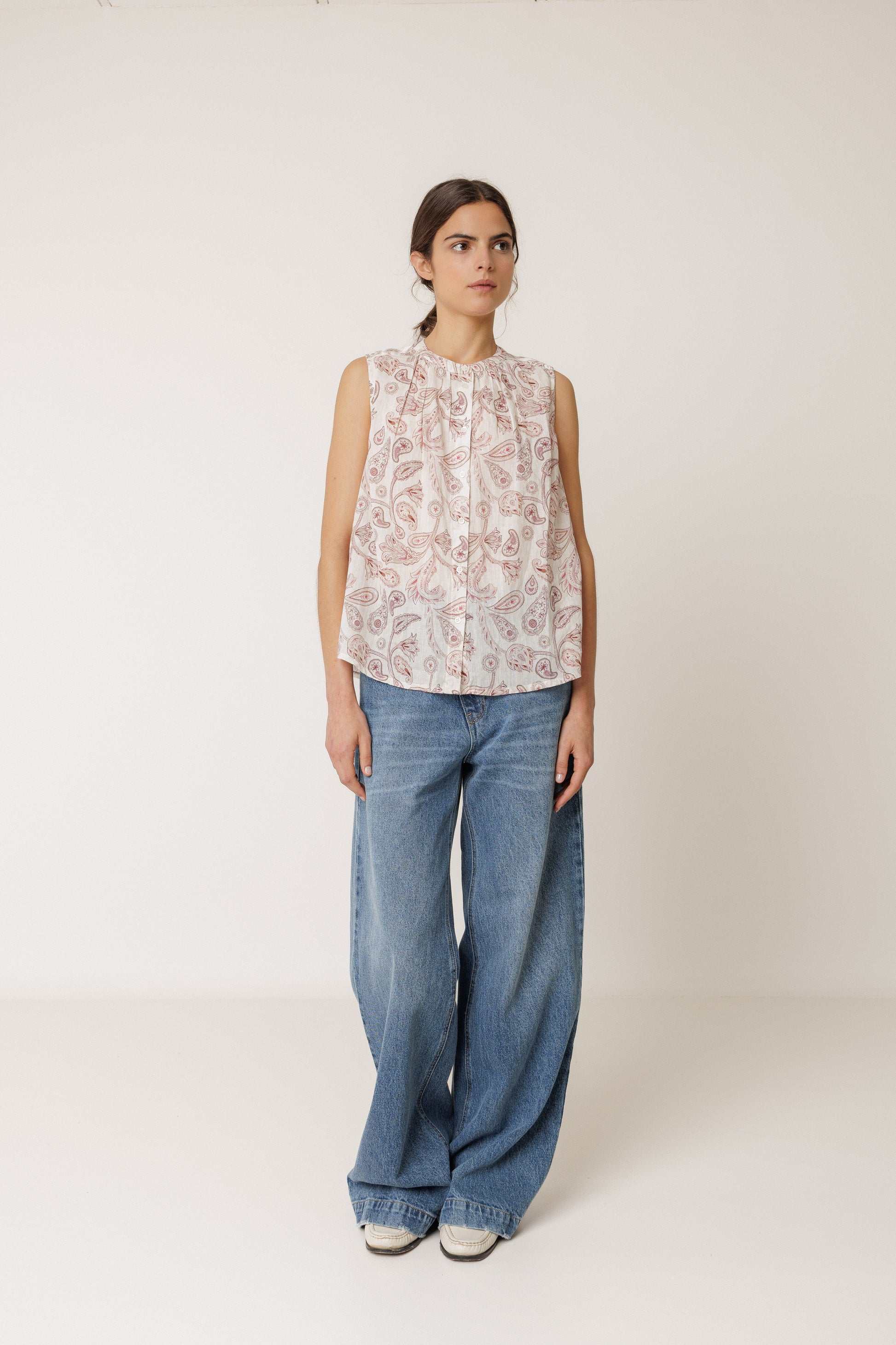 Woman wearing a sleeveless floral top and blue jeans on a white background