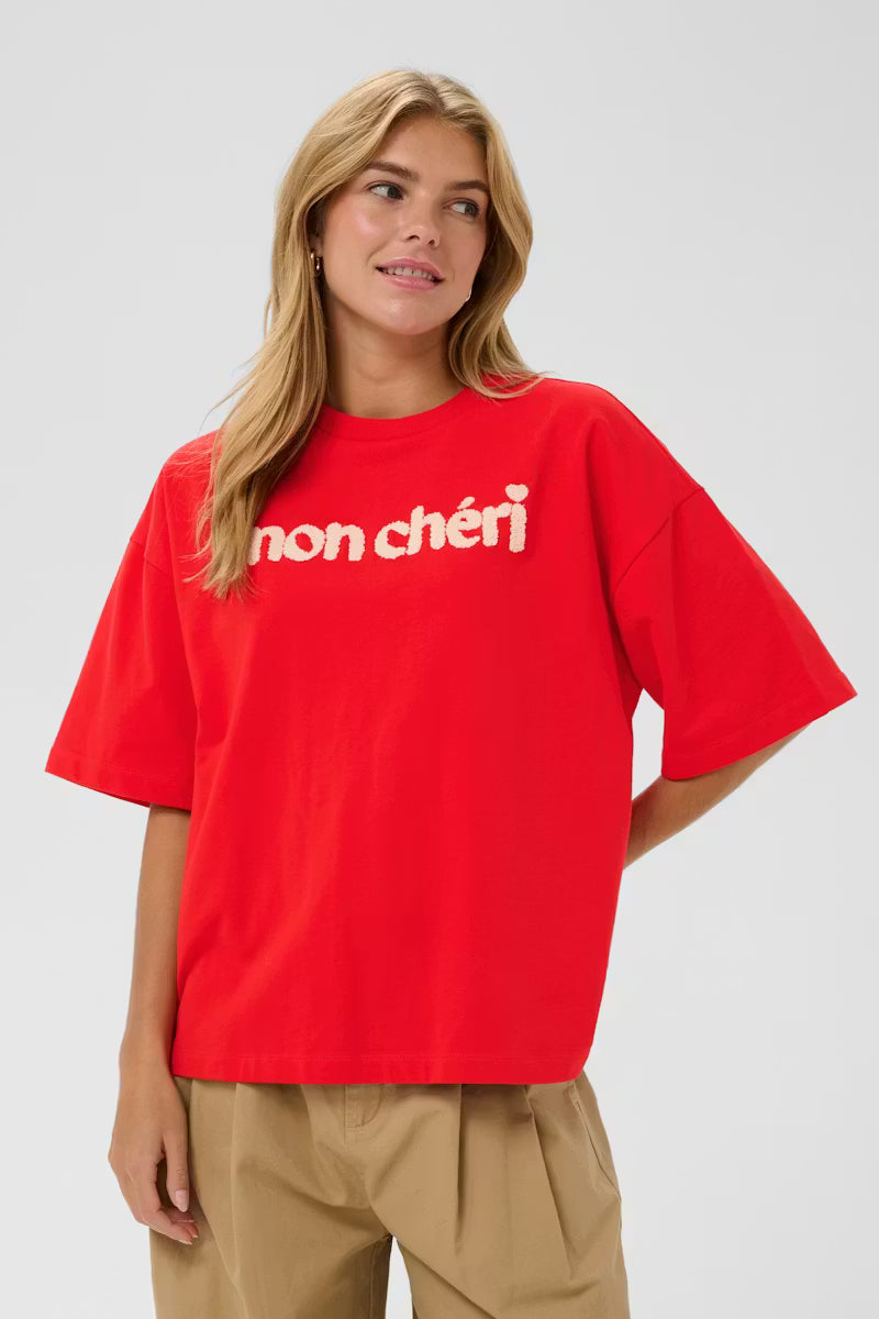 Woman wearing a red t-shirt with 'non cheri' text on a plain background