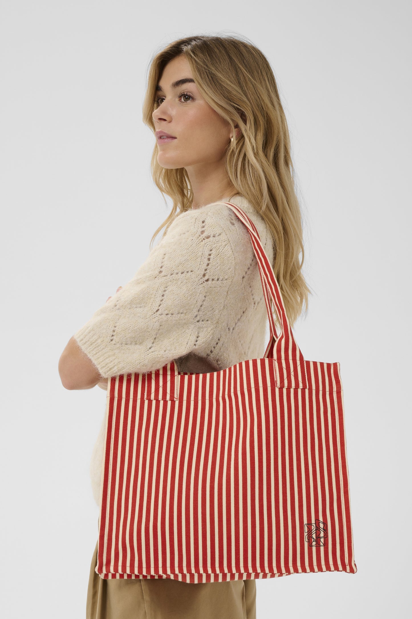 Woman holding a red and white striped bag against a plain background