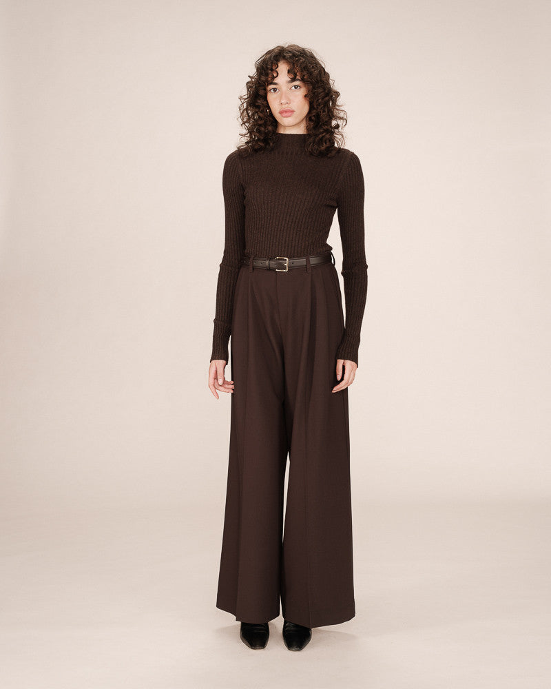 Woman wearing a brown turtleneck and wide-leg pants on a beige background