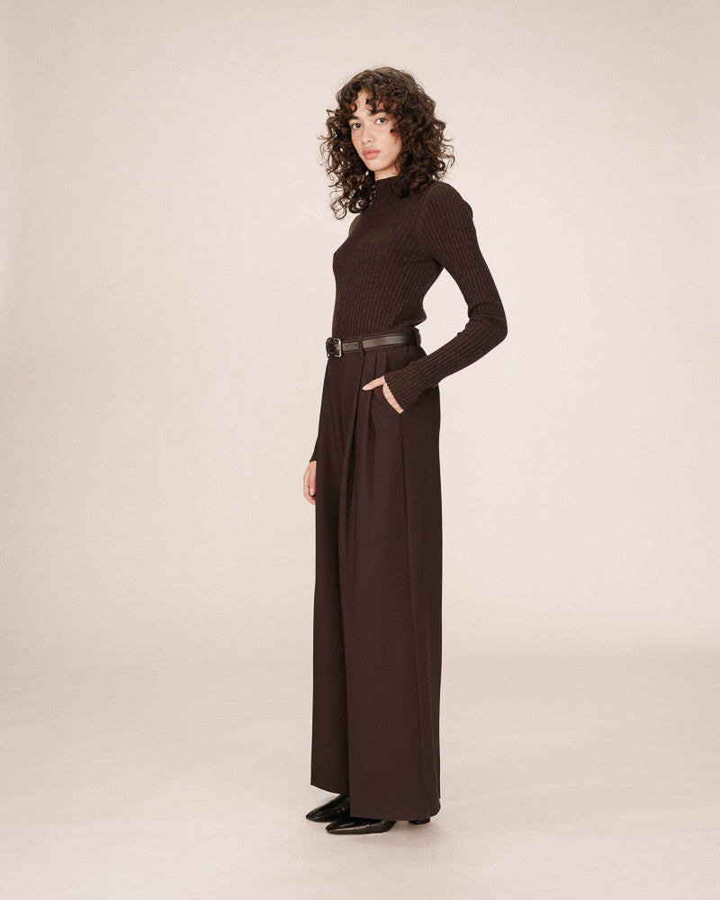 Woman wearing a long brown dress with a belt on a beige background