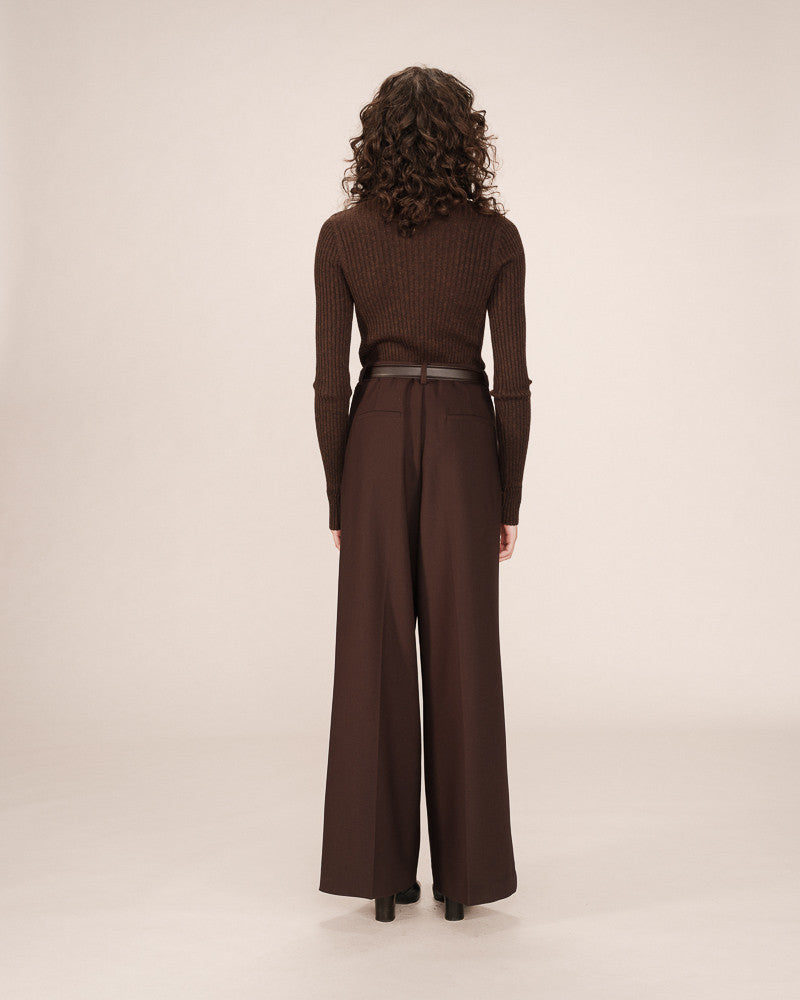Woman wearing a brown ribbed top and wide-leg pants on a beige background
